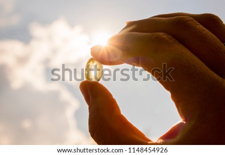 Vitamin D keeps you healthy while lack of sun. Yellow soft shell D-vitamin capsule against sun and blue sky on sunny day. Cure concept. Royalty-Free Stock Photo #1148454926