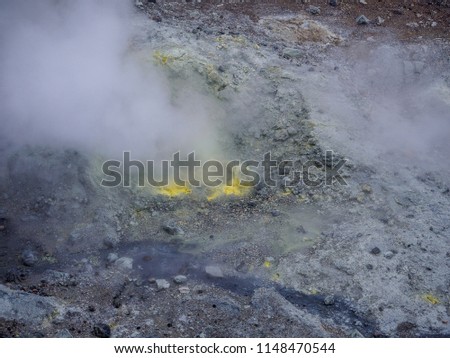 Volcanic creek with boiling water running through mountain terrain with stones, smoking fumaroles and yellow sulfur deposits 