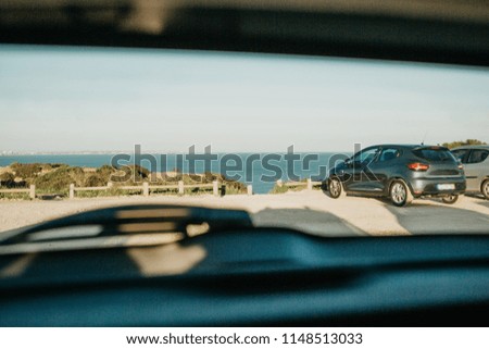 View through the rear window of the car to the parking lot with other cars and the sea or the ocean in summer. Conceptual picture of summer travel by car.
