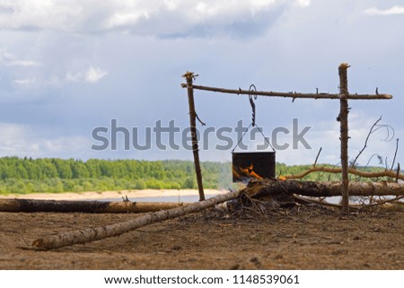A bonfire and a fireplace with a pot in the fire. Tourist fire on the river bank in gloomy gray weather. The pot hangs on the hook over the fire. Preparation of camp food