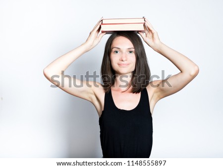 portrait of a beautiful young woman holding books on her head, isolated studio photo on a gray background