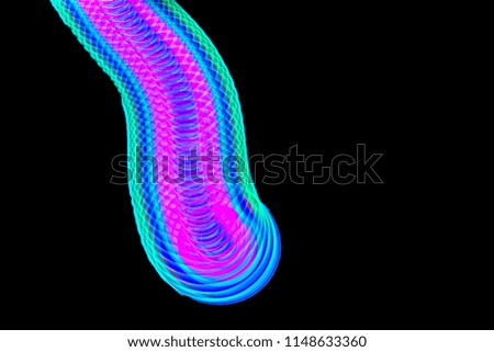 Long exposure, multicolor Led light painting of a spinning top on abstract black background.