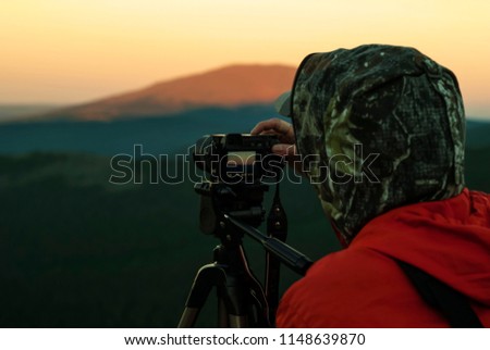 woman photographer takes a picture of a dawn in the mountains by camera on a tripod

