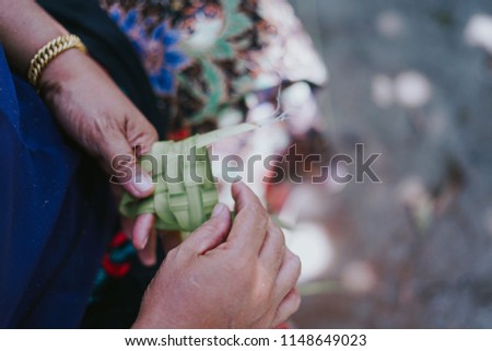 Close up shot of old woman's hand making ketupat or rice dumpling case using coconut leave.