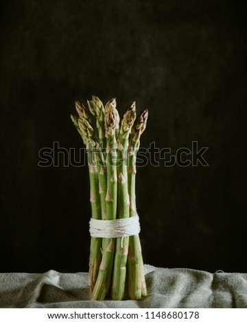 A bundle of green asparagus on linen against a black background with Rembrandt lighting