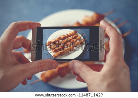 Man hands making food photography of lunch with smartphone for social networks. Blogger shoot chicken skewers for instagram.