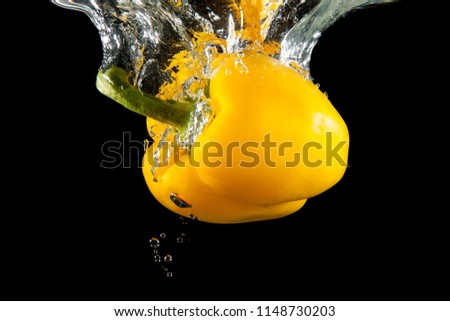 Yellow fresh vibrant pepper splashing into water