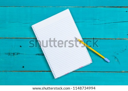 Spiral notebook with yellow pencil on rustic antique teal blue wood desk; above view looking down business background with white copy space