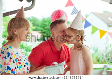 Portrait of happy grandparents celebrating birthday with their pretty little granddaughter on colorful decorated terrace