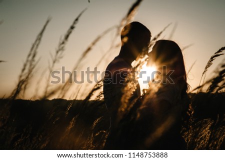 Silhouette young couple hugging and kissing in autumn at an outdoor on park on the background field, grass over sunset. Man and woman. Concept of friendly family. upper half. Closeup. Place for text.
