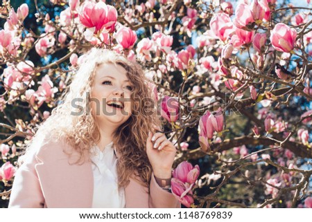 curly-haired laughing woman in a pink coat enjoying the spring and warmth in the park in the sun