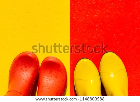 Red wet background with yellow rubber boots and yellow background with red boots on it. The view from the top. The concept of "Autumn is coming"