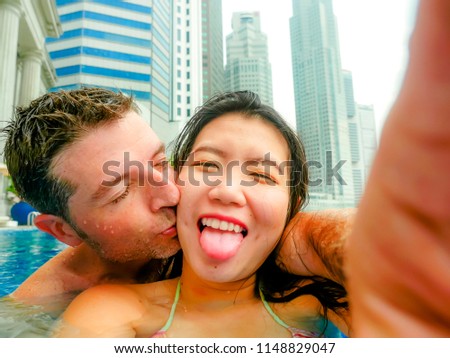 young happy and attractive playful couple taking selfie picture together with mobile phone at luxury urban hotel kissing at infinity pool enjoying holidays honeymoon in diversity ethnicity and love