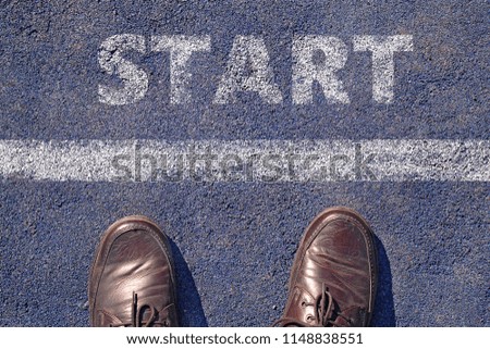 man feet in brown leather shoes standing before shabby sign start written on asphalt, top view