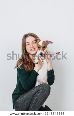 Studio portrait of a cute young woman smiling and hugging her puppy jack russell terrier dog. Love between dog and owner.Isolated on white background.