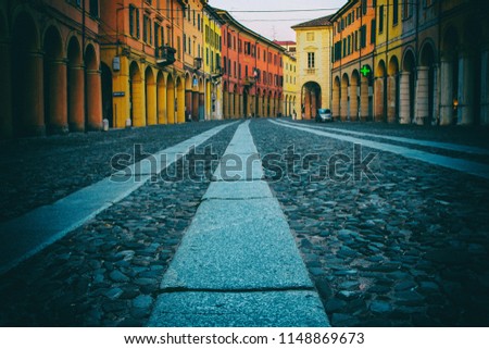 Low angle photo of a stone street in an old Italian town with colorful houses and business edifices with a pharmacy. No people.