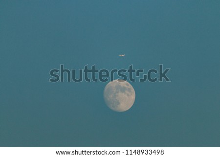 Plane floating over full moon on clear sunset sky.