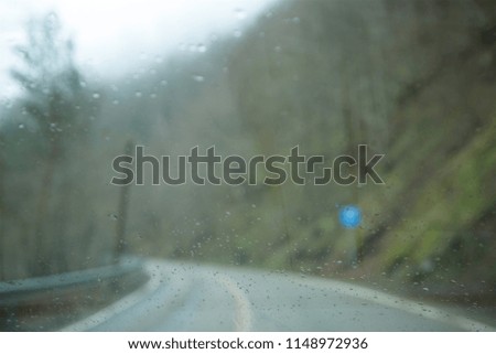 Defocused blurred abstract background of forest roads in the side of the road. Focus on rain drops on the windshield of car.