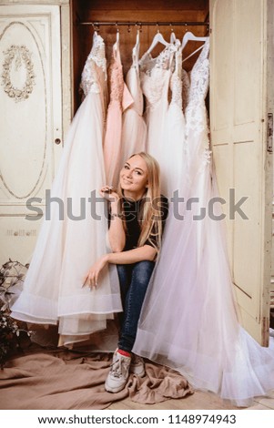 Woman in casual clothes sitting near vintage wardrobe with many wedding dresses