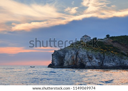 Lonely little house on a stone precipice over the sea against the backdrop of sunset. A small fishing boat in the open sea. A beautiful seascape on the Adriatic.