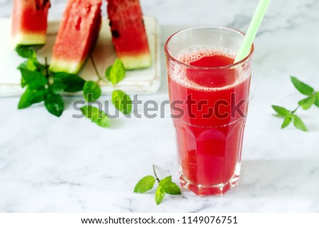 Cold watermelon lemonade with mint in a glass cup and slices of watermelon on a light background.