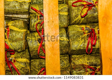 Small pieces of wood in yellow bags closed with a red string arranged symmetrically on a wooden container in a warehouse, pieces of wood to use in winter in fireplaces or campfires
