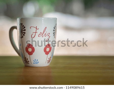 White coffee mug with flower pictures and the Spanish word "feliz" (happy)