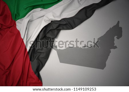 waving colorful national flag of united arab emirates on a gray map background.