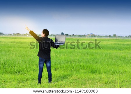 Man holding computer in green field under blue sky.Blogger Sky and Clouds