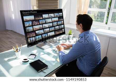 Young male editor searching photos on computer in office