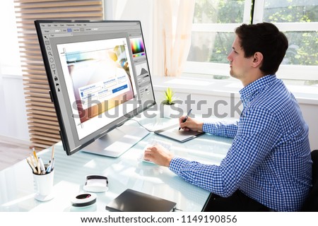 Young male editor using graphic tablet for sketch while working on computer