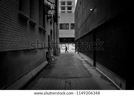 Black and white photo of man walking in dark alley 