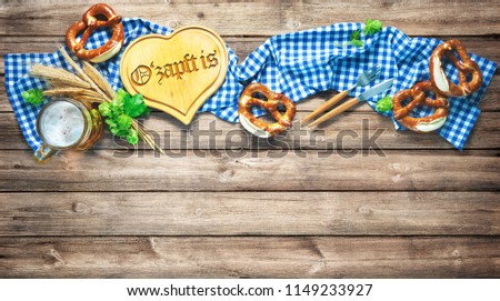 Rustic background for Oktoberfest with white and blue fabric, hop, silverware, beer glass and pretzels on wooden table. Menu card for Restaurants. Translation: "The beer is tapped"