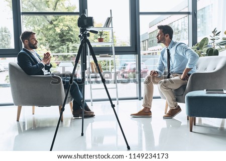 Filming interview. Two young men in smart casual wear talking while making new video indoors         Royalty-Free Stock Photo #1149234173