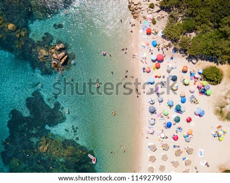 View from above, aerial view of an emerald and transparent Mediterranean sea with a white beach full of colored beach umbrellas and tourists who relax and swim. Costa Smeralda, Sardinia, Italy.