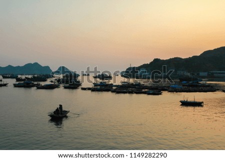 Cat Ba Island Vietnam, boats on the water with warm orange glowing sunset in the background. Ocean horizon with small islands in the background. Largest island in Halong Bay, ocean water background