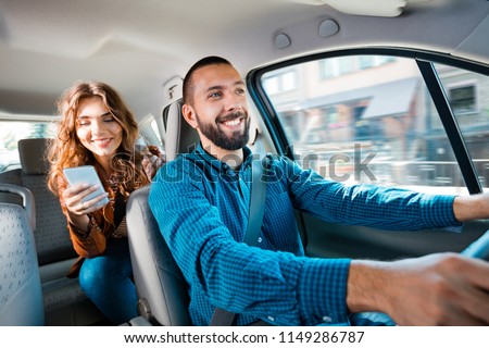 Similing driver talking with female passenger. Woman holding mobile phone in hand. Royalty-Free Stock Photo #1149286787