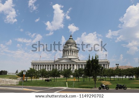 A picture of the Utah state capitol building with two motor cycles parked in front and people sitting on a bench