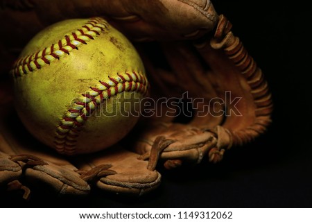 A yellow softball in an old, brown, glove.