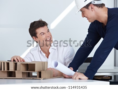 Architect with hardhat and blueprint talking to his employees in the office