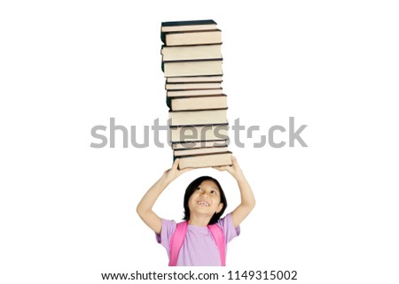 Picture of cute schoolgirl lifting a pile of books while standing in the studio, isolated on white background