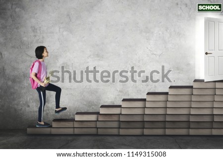 Picture of Asian schoolgirl carrying a trophy while walking on book stairs toward a school door