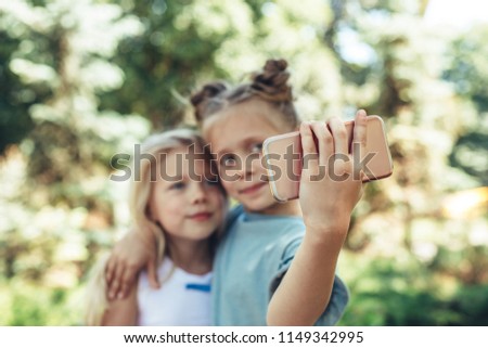 Focus on kid hand holding smartphone outside and making selfie. Little girls are happy and delighted amusing themselves on nature