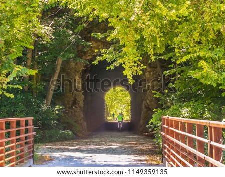 Early fall view of  the tunnel on a recreational trail stretching along the Missouri River; Missouri, Midwest; bicyclists in the distance Royalty-Free Stock Photo #1149359135