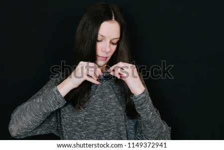 Woman brunette attaches the lavalier microphone to the blouse on a black background.