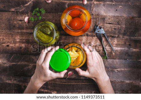 Homemade jars of pickled fresh cucumbers, juicy tomatoes, sweet zucchini on a wooden background. Stock of food. Autumn concept. Top view