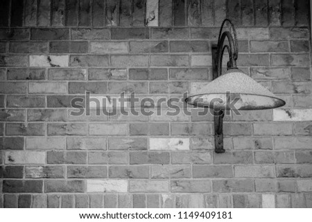 A black and white photo of a rusty, retro lamp attached to a grungy, gritty brick wall with bricks of different shades framed by a shadow vignette.