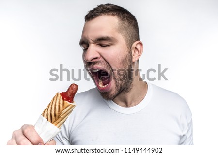 A picture of man that likes oily fast food. On this picture he wants to bite a big piece from fat hot dog. Man looks weird but brutal. Isolated on white background.