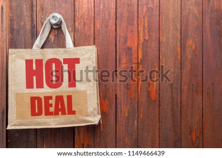 Hot deal sign on Nature eco-friendly grocery shopping bag, Jute tote bag with self handles hanging on red old wooden doll background