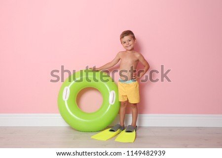 Cute little boy with inflatable ring wearing flippers near color wall